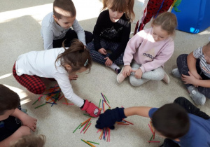 Dzieci w grubych rękawicach przekładają do siebie kolorowe patyczki